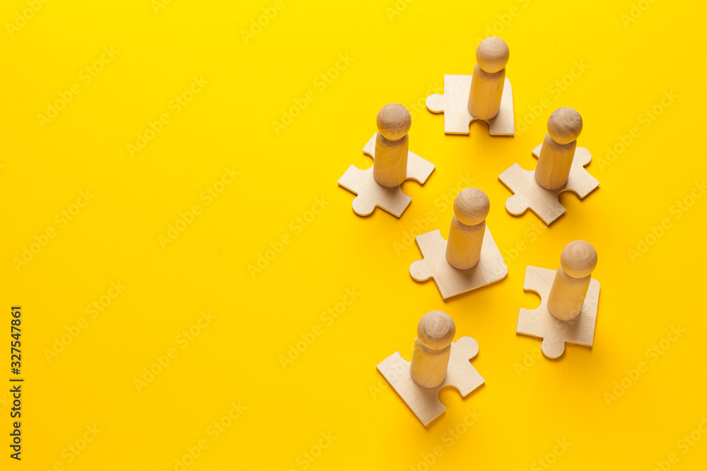Wooden figures on puzzles on yellow background as a symbol of team building. Organization group people in business. Cooperation and partnership. Wooden figures on puzzles on yellow background as a symbol of team building. Organization group people in business. Cooperation and partnership.