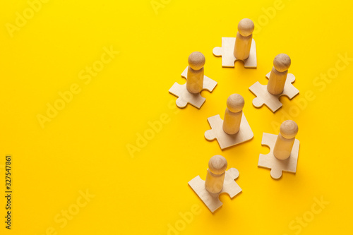 Wooden figures on puzzles on yellow background as a symbol of team building. Organization group people in business. Cooperation and partnership.