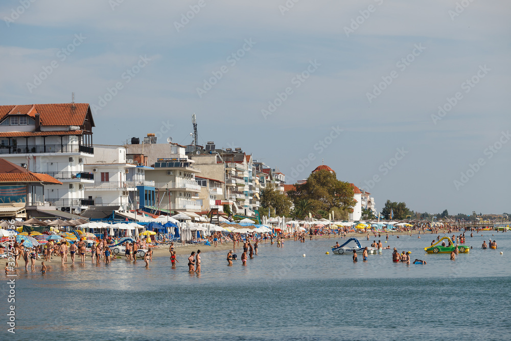 PARALIA, GREECE - SEPTEMBER 10, 2018: Beach scene. People swimming and sunbathing on the comfort shallow water coast full of budget hotels