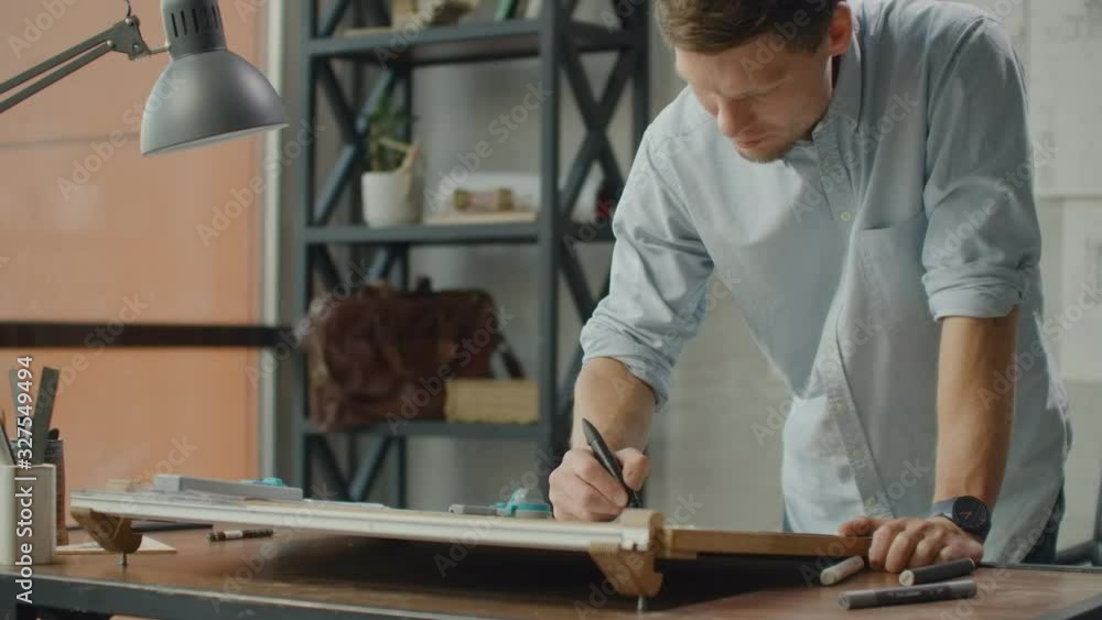 Engineer works in a bright office with a large window, concentrates and draws blueprints. Workplace of an architect or designer: loft style, minimalistic interior, drawings. Engineer works in a bright office with a large window, concentrates and draws blueprints. Workplace of an architect or designer: loft style, minimalistic interior, drawings.