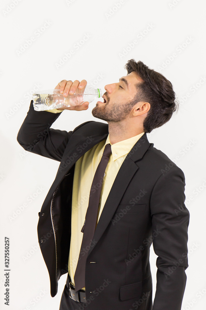 A handsome young businessman standing alone, drinking water from a clear plastic bottle on a white background. A handsome young businessman standing alone, drinking water from a clear plastic bottle on a white background.