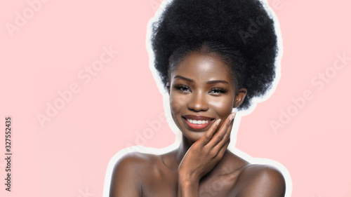 Pretty Afro American Woman Isolated On Pink Color Background, Beautiful Girl With Clean Fresh Skin Carefully Touches Her Face With Her Hand, Copy Space Is Located On The Left