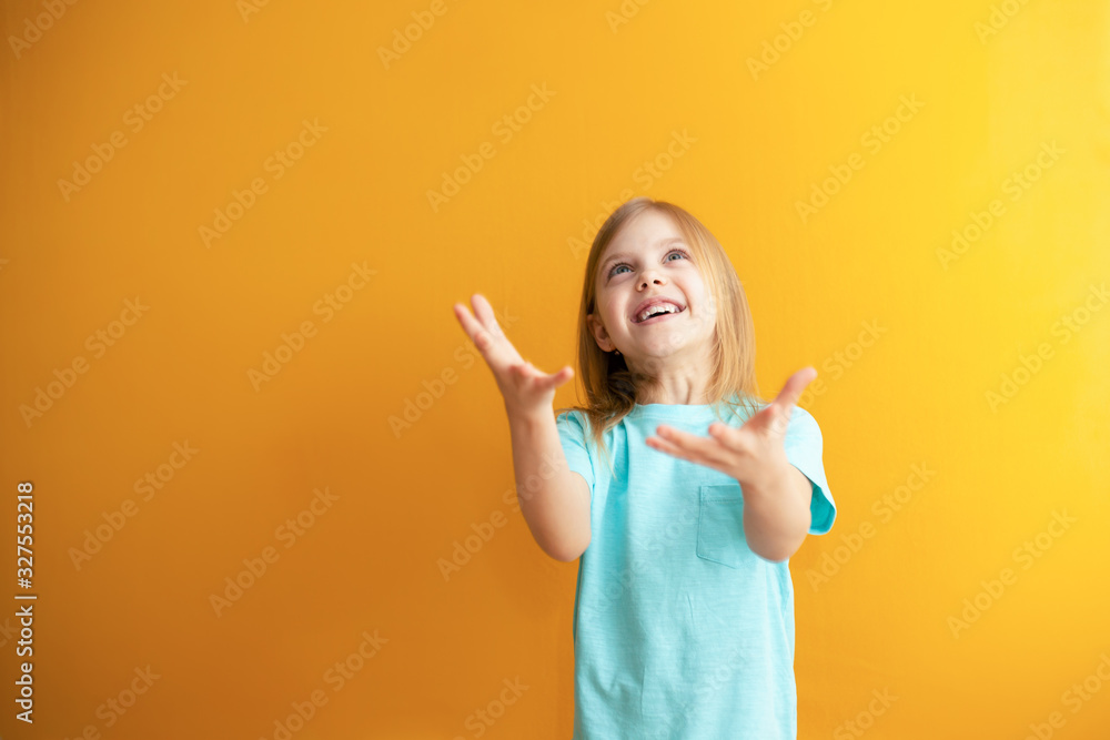 cute baby on an orange background, 6-8 years old, baby girl catches something or is ready to catch falling from above cute baby on an orange background, 6-8 years old, baby girl catches something or is ready to catch falling from above