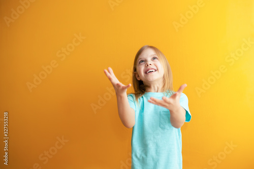 cute baby on an orange background, 6-8 years old, baby girl catches something or is ready to catch falling from above