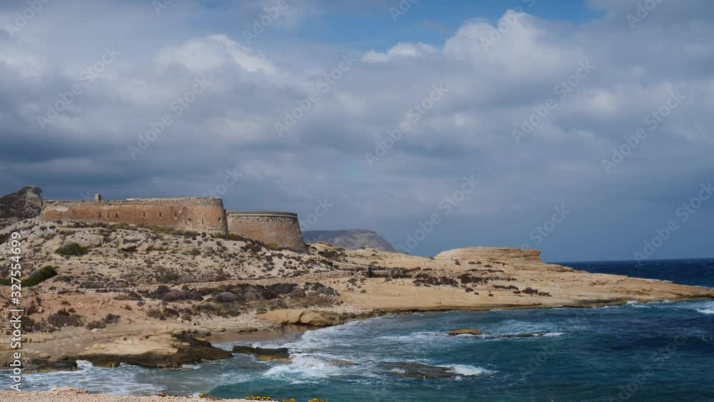 Castle San Ramon above beach of El Playazo, Cabo de Gata, province AlmerĂa, Andalusia Spain. Rocky sea shore with waves splashing in slow motion. Tourist site Castle San Ramon above beach of El Playazo, Cabo de Gata, province AlmerĂa, Andalusia Spain. Rocky sea shore with waves splashing in slow motion. Tourist site