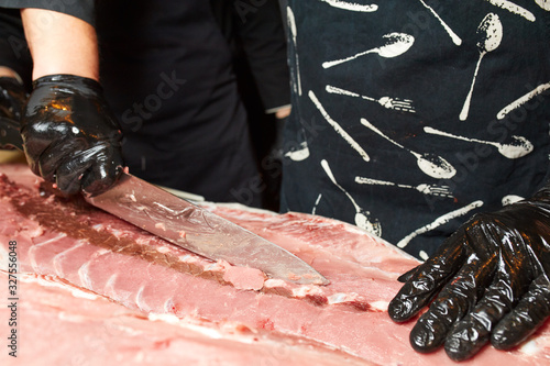 cuts the meat of a big fish with a large knife, hands in black gloves hold a knife and cut tuna photo