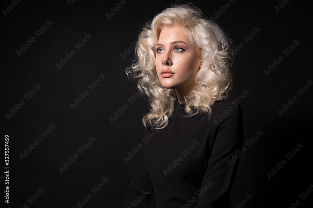 Dreamy blonde young woman with wavy hair isolated on black background