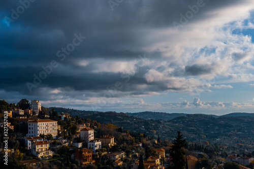 The panoramic cityscape view of a Côte d'Azur town's houses and the Alps mountains next to the Meditarrenean sea under a moody cloudy sky (Grasse, France)