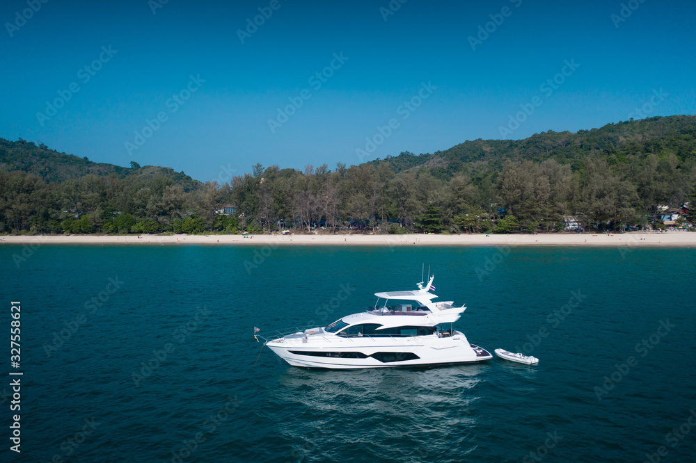 Aerial drone view of luxury white yacht in the blue sea with beach in the background. Travel concept