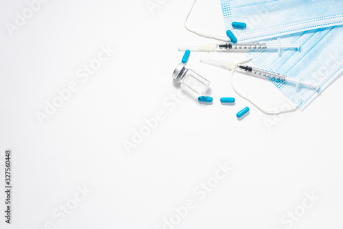 Flat lay overhead view of sterile medical masks, vial with vaccine, thermometer and two syringes isolated on white background with copy space for your design. vaccination and health care concept.