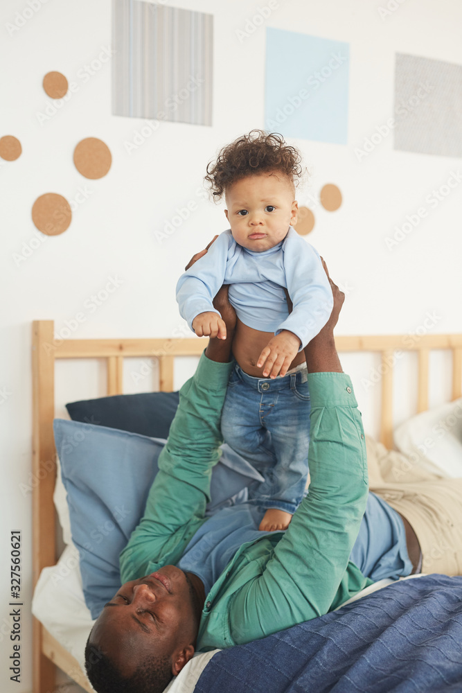Fototapeta premium Portrait of happy African-American father playing with little son while lying on bed at home