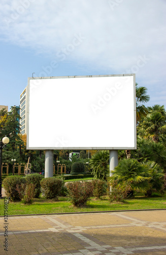Blank street billboard poster in the park on the background of tropical plants. information banner, copy space for text.