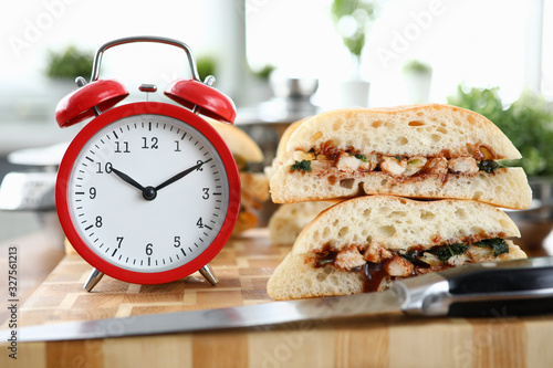 Red alarm clock with sandwich stands on wooden table closeup background. Fast food delivery concept.