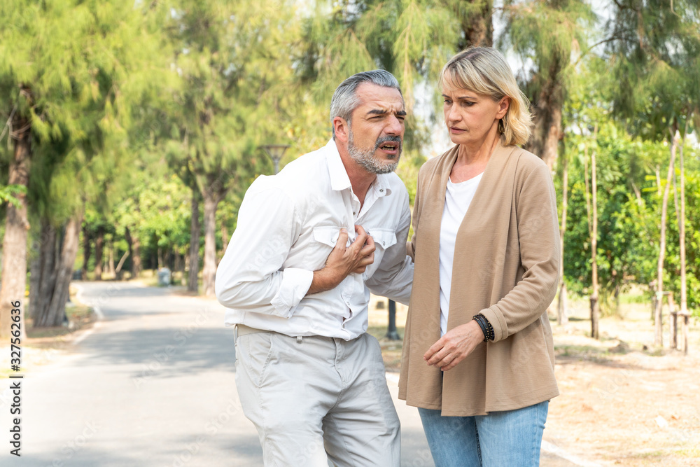Caucasian senior man suffering, clutching and having chest pain cause from heart attack while walking in the park with his wife, older woman care and support husband, health problem and insurance Caucasian senior man suffering, clutching and having chest pain cause from heart attack while walking in the park with his wife, older woman care and support husband, health problem and insurance