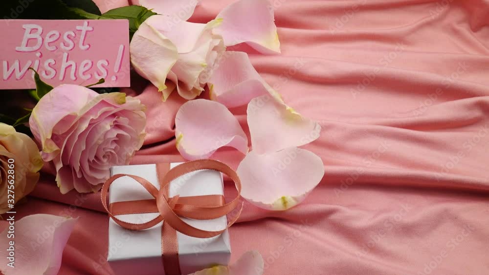 Bouquet of pink roses, pale pink rose petals, gift in a box, and Best Wishes card lay on a pink satin, background Bouquet of pink roses, pale pink rose petals, gift in a box, and Best Wishes card lay on a pink satin, background