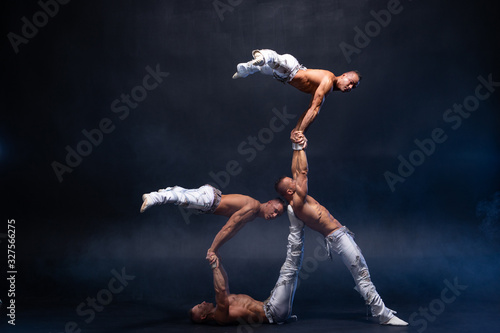 Four muscular man perform difficult acrobatic tricks on black studio 