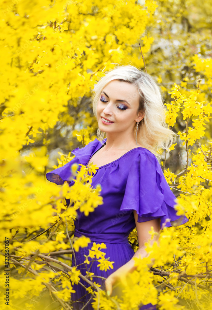 portrait of a girl on a background of yellow flowers. Spring photo with a beautiful woman in a purple dress with blooming forsythia. The concept of perfumery and cosmetics portrait of a girl on a background of yellow flowers. Spring photo with a beautiful woman in a purple dress with blooming forsythia. The concept of perfumery and cosmetics