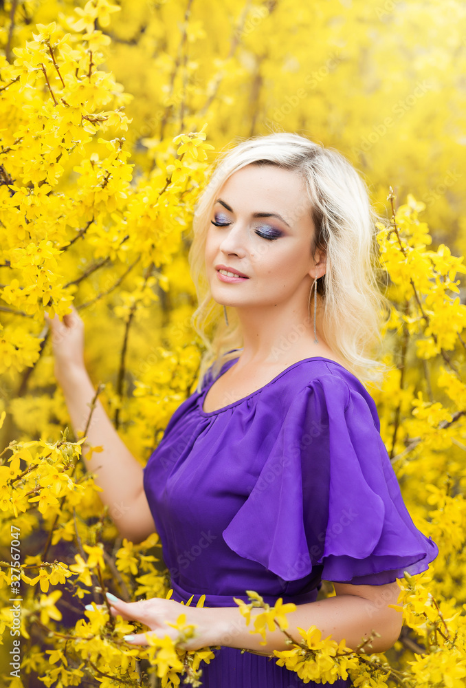portrait of a girl on a background of yellow flowers. Spring photo with a beautiful woman in a purple dress with blooming forsythia. The concept of perfumery and cosmetics portrait of a girl on a background of yellow flowers. Spring photo with a beautiful woman in a purple dress with blooming forsythia. The concept of perfumery and cosmetics