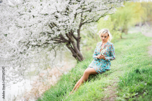 Romantic beautiful woman in a Park on the lake sits on the background of a flowering tree. Spring photo with a beautiful girl in a floral dress
