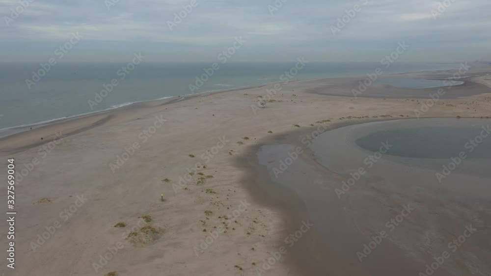 Aerial view that slowly winds around a large beach with a few people walking in the distance Aerial view that slowly winds around a large beach with a few people walking in the distance
