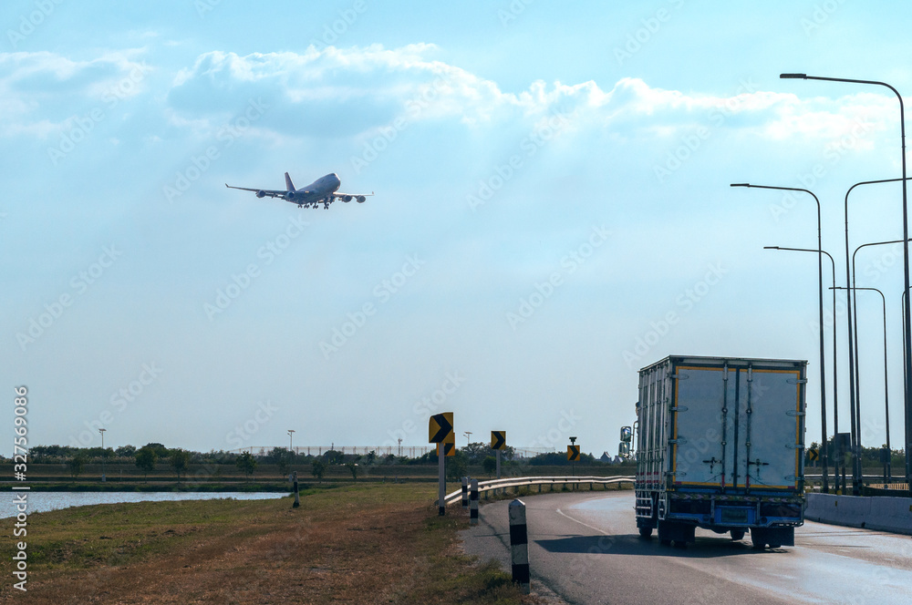 Fototapeta premium Flying Passenger Jet Plane on The Sky over The Container Truck Running on The Road