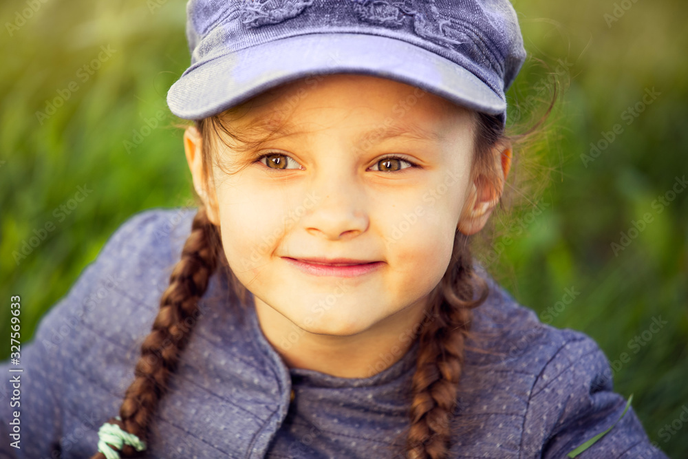 Happy smiling kid girl looking on the glass in blue clothing on summer green background. Closeup Happy smiling kid girl looking on the glass in blue clothing on summer green background. Closeup
