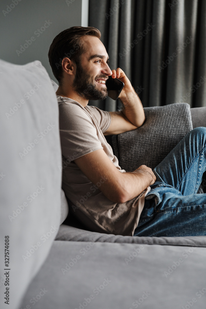 Happy young man indoors on sofa talking by phone. Happy young man indoors on sofa talking by phone.