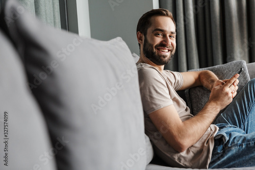 Positive young man indoors at home on sofa