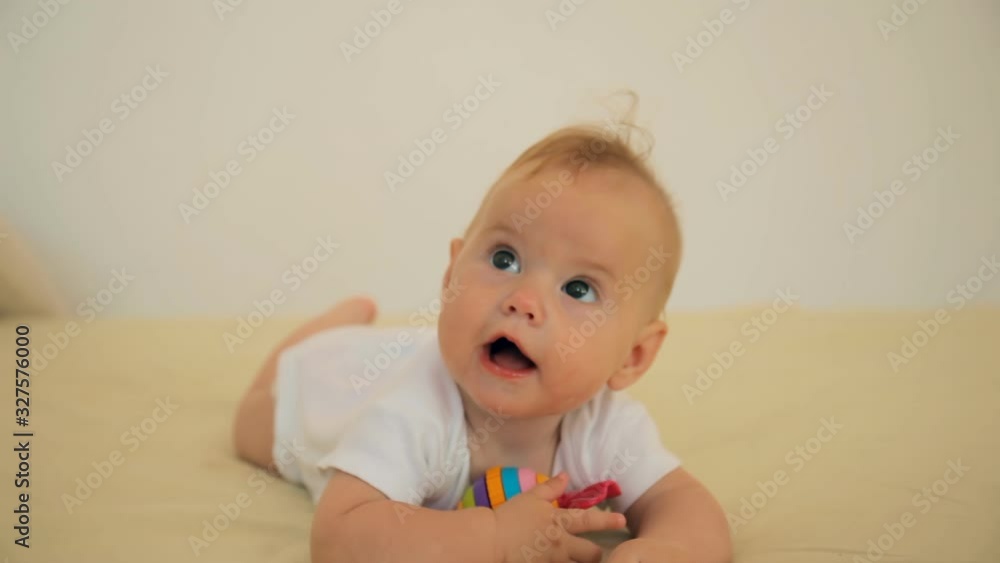 Portrait of happy smile baby relaxing on the bed gnaws a toy looking at camera Portrait of happy smile baby relaxing on the bed gnaws a toy looking at camera