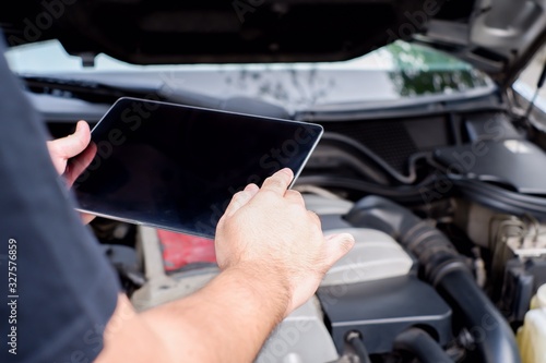 The mechanic is customizing the car with a tablet. Modern technology concepts and the automotive industry.