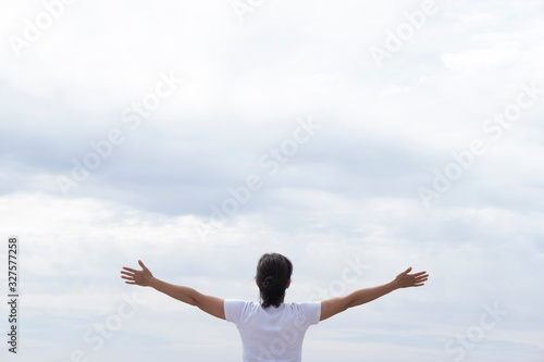 woman in white t-shirt raising her arms facing the sea