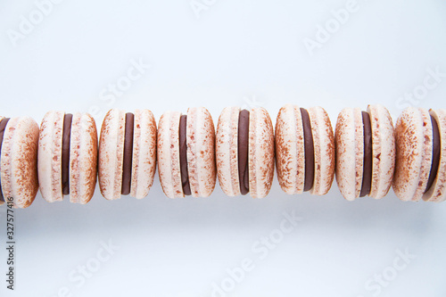 French dessert macarons are in a line (row). Macarons are powered with cocoa powder and filled with dark chocolate ganache On a white background. Top view.