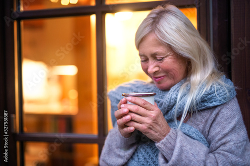 Senior woman with coffee standing outdoors on terrace, resting.