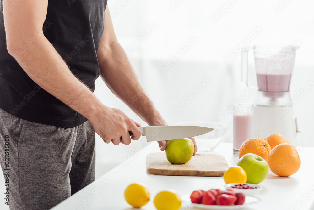 cropped view of man cutting apple near fresh fruits and smoothie