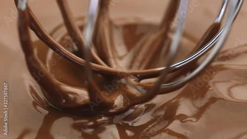 Mixing smooth delicious melted dark or milk chocolate with a whisk that spins. Closeup. Organic chocolate icing to prepare confectionery. Pastry bakery patisserie preparing pralines or chocolates.