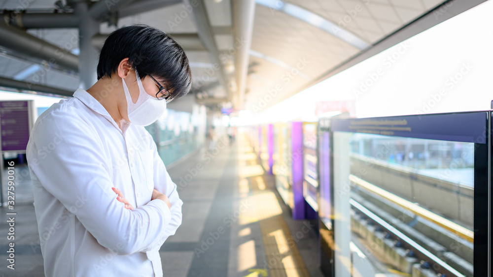Asian man wearing face mask at skytrain station or urban train platform. Wuhan coronavirus (COVID-19) outbreak prevention in public transportation. Health awareness for PM2.5 air pollution protection. Asian man wearing face mask at skytrain station or urban train platform. Wuhan coronavirus (COVID-19) outbreak prevention in public transportation. Health awareness for PM2.5 air pollution protection.