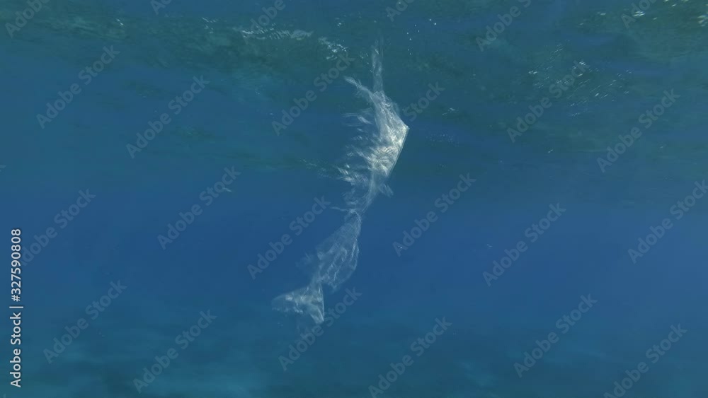 A piece of plastic bag slowly drifts in blue water, gradually collapsing and turns into microplastics. Underwater plastic pollution of the ocean. Plastic garbage environmental pollution problem. A piece of plastic bag slowly drifts in blue water, gradually collapsing and turns into microplastics. Underwater plastic pollution of the ocean. Plastic garbage environmental pollution problem.