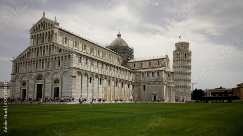 Pisa cathedral with the leaning tower of Pisa, view from across a grassy meadow, Italy