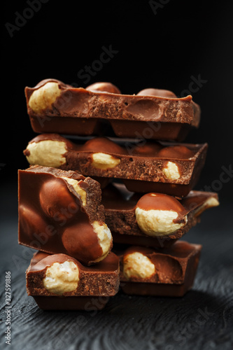 Chocolate with hazelnut in the form of a tower on a dark background. Pieces of milk chocolate with nuts.