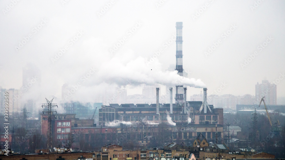 old factory in the fog, with pipes emitting industrial waste in the form of smoke, in the middle of the city, in the foreground and background residential buildings
