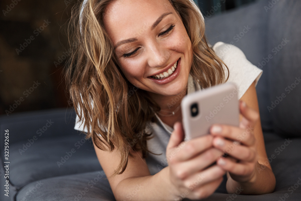 Image of smiling blonde woman using cellphone and wireless headphones - obrazy, fototapety, plakaty 