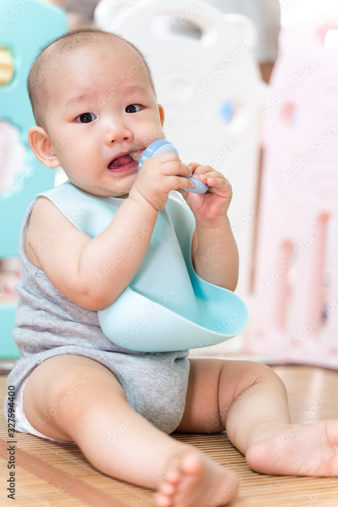An Asian baby sits in a pen, biting a pacifier An Asian baby sits in a pen, biting a pacifier