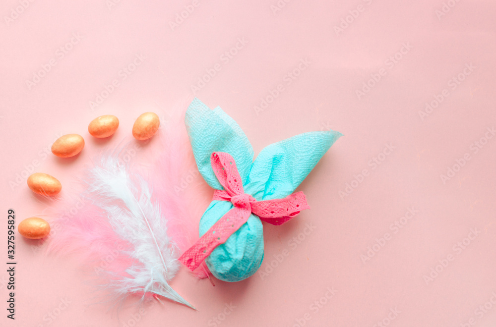 Egg gift in green paper packaging and with pink ribbon Easter Bunny wrap idea. Chocolate dragee white and gold color, multicolor colorful feathers. Minimal concept. Flat lay, Copy space, top view Egg gift in green paper packaging and with pink ribbon Easter Bunny wrap idea. Chocolate dragee white and gold color, multicolor colorful feathers. Minimal concept. Flat lay, Copy space, top view