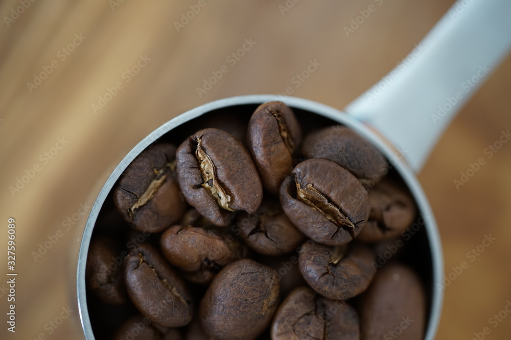 Naklejka premium Kaffeebohnen in einem Kaffeedosierlöffel auf einem Holzbrett