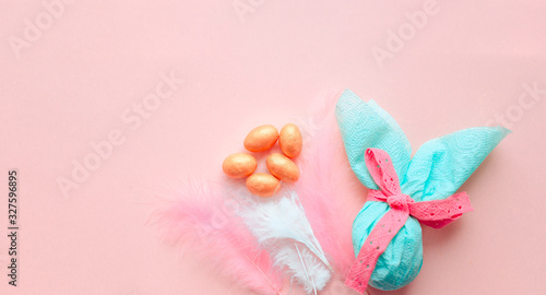 Egg gift in green paper packaging and with pink ribbon Easter Bunny wrap idea. Chocolate dragee white and gold color  multicolor colorful feathers. Minimal concept. Flat lay  Copy space  top view