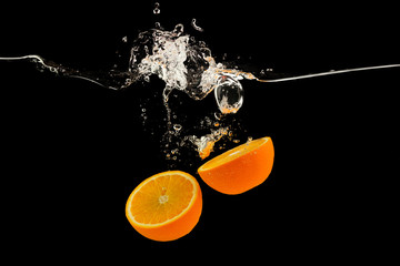 Falling citrus fruits. Orange halves splattering into water on black background