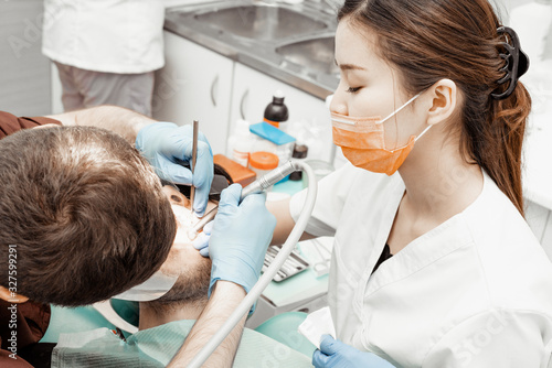 A young male dentist doctor treats a patient. Medical manipulations in dentistry, surgery. Professional uniform and equipment of a dentist. Healthcare Equipping a doctor’s workplace. Dentistry