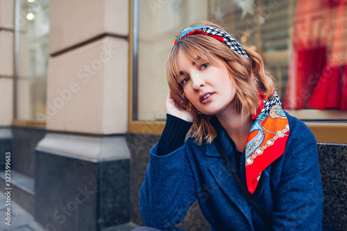 Valokuvatapetti Stylish woman wearing headband scarf blue coat by shop on street
