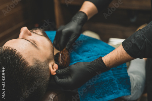 Haircut head and beard in a barbershop. Barber puts on and combs the client’s beard. The process of creating a hairstyle and styling a beard for men. A man in a barbershop. Selective focus
