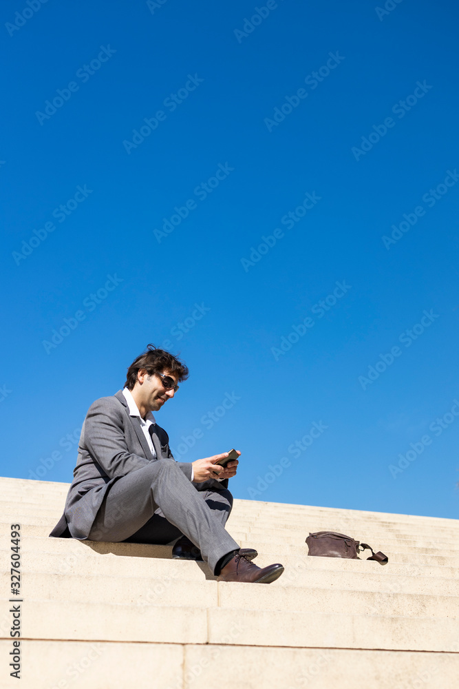Smiling young business man sitting on steps with a cellphone
